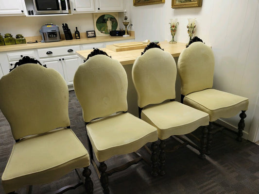 A set of six vintage beige dining chairs with ornate wood trim on the backs, displayed in a room setting.